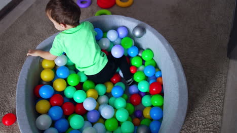 dark-haired toddler boy sitting in the dry pool. kid throws the balls around and climbs out of the basin. top view.