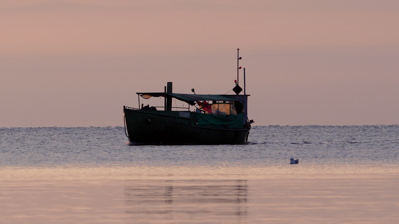 Fishing boat rests on a calm sea under soft pastel sky at sunrise, with seagull nearby
