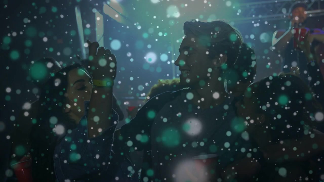 Trio at gig talking as lights, singer sparking smiles, flakes hiding faces, red cups, man turning