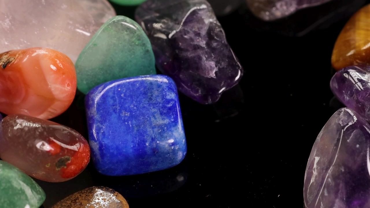 Pedras preciosas lapidadas vibrantes caem e se acomodam em um arranjo colorido contra um fundo escuro.