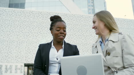 And-Female-Colleagues-Sitting-Outdoors,-Looking-At-Laptop-Screen-And-Talking-About-Something