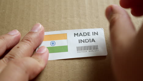 Manos-Aplicando-La-Etiqueta-De-La-Bandera-Hecha-En-India-En-Una-Caja-De-Envío-Con-Un-Código-De-Barras-De-Primera-Calidad-Del-Producto.