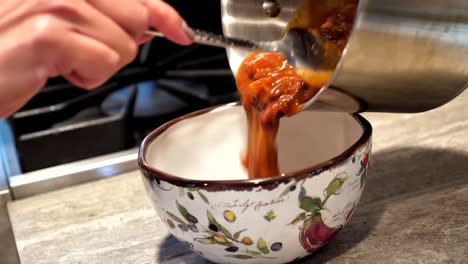 closeup of person pouring hot chili out of pot, into bowl, static shot