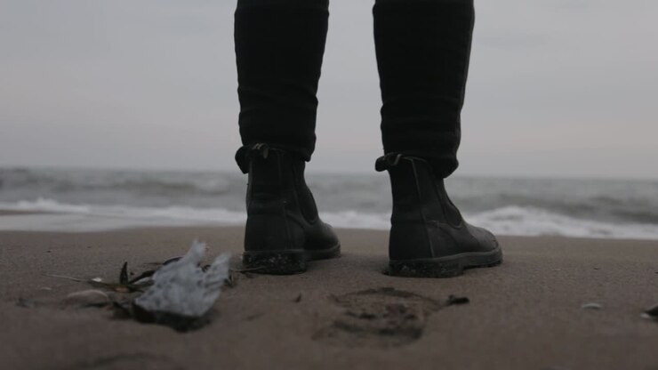 A Man Standing By The Shore Wearing Black Shoes With Soft Waves Touching HIs Sole - Close Up Shot