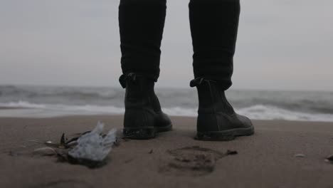 a man standing by the shore wearing black shoes with soft waves touching his sole - close up shot