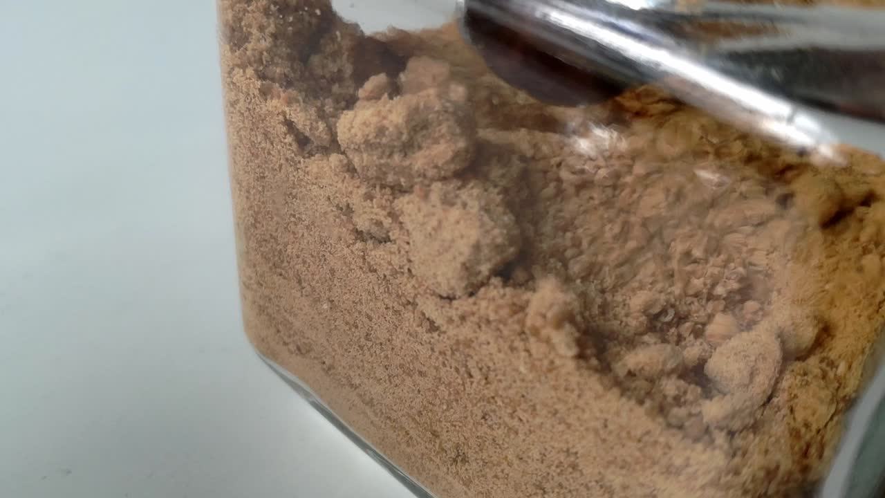Close-up of brown raw cane sugar being scooped, showing texture and fine granules