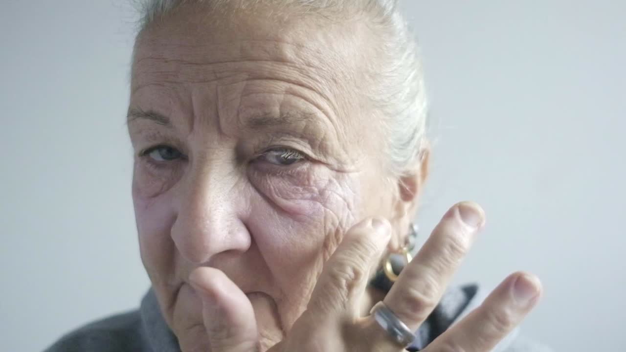 Elder caucasian woman puts herself cream makeup, closeup shot portrait face look at camera, mirror
