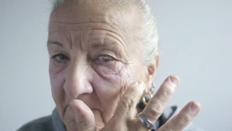 elder caucasian woman puts herself cream makeup, closeup shot portrait face look at camera, mirror