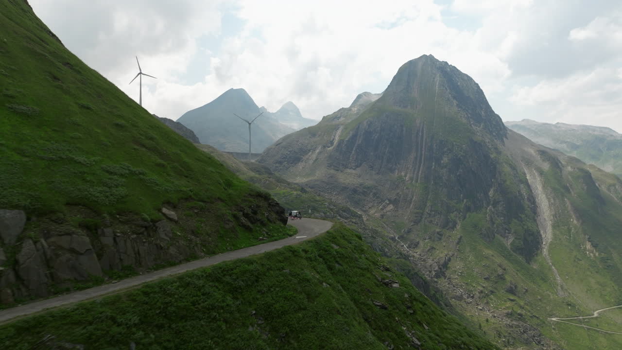 vuelo aéreo a lo largo de la sinuosa carretera de montaña grimsel pass con revelación de turbinas eólicas en la línea de la cresta en segundo plano
