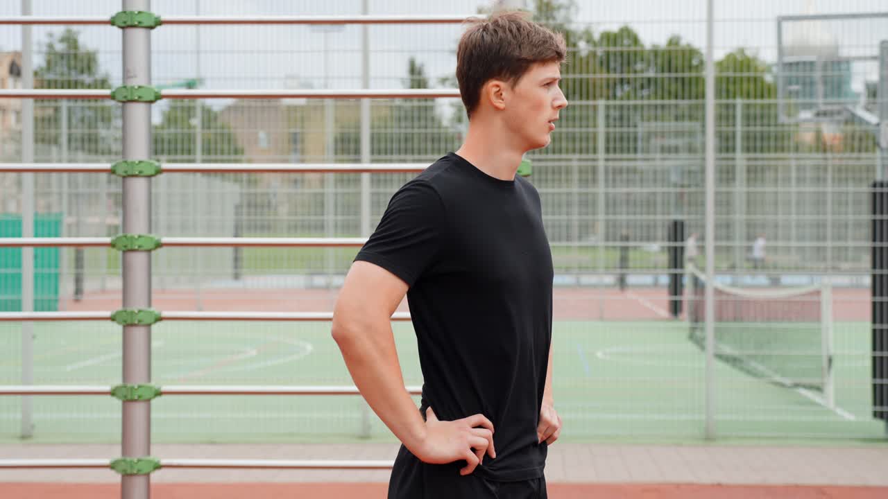 Young man pausing during an outdoor workout on a sports ground, embracing an active lifestyle and staying fit for good health and wellness, slow motion, static camera shot