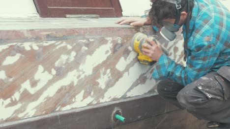 sanding a wooden boat hull using an orbital sander