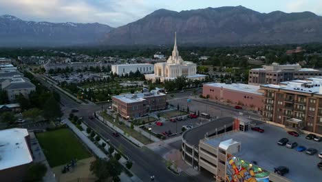 LDS-Mormon-Temple-in-Ogden-Utah-drone-flight-flying-at-dusk-on-beautiful-summer-night-wide-shot-a-quarter-mile-away-flying-towards-Angel-Moroni-on-top-of-temple-with-mountains-in-background