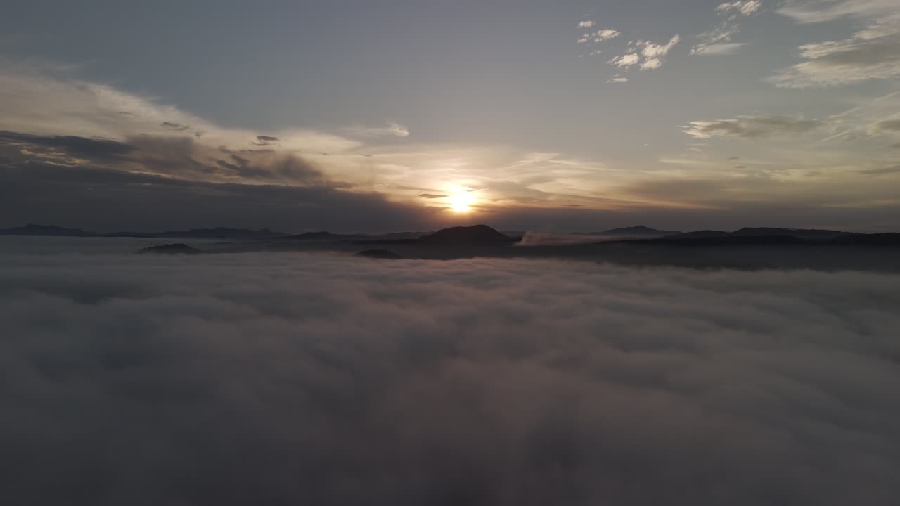 escena adelante por encima de las nubes con una puesta de sol y montañas en el fondo