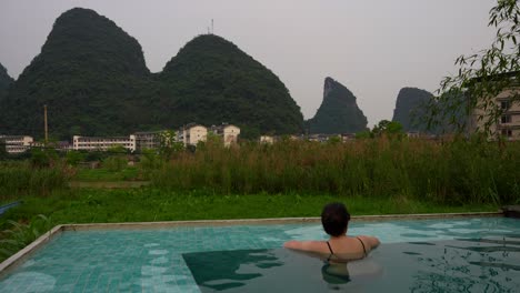 caucasian tourist woman in outdoor pool contemplating karst mountains of yangshuo, china