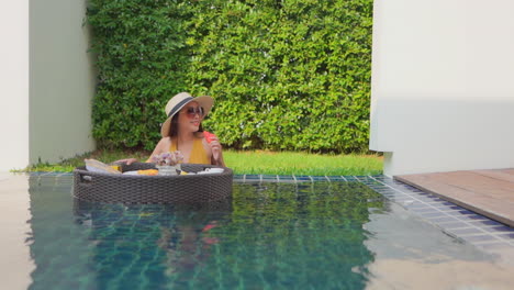 a woman in a swimming pool looks over the floating service tray choosing a piece of fruit to eat