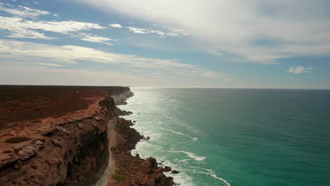 Aerial-drone-shot-of-epic-cliff-range-with-crystal-clear-ocean-during-sunlight