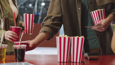 primer plano de una pareja irreconocible comprando entradas para el cine, palomitas de maíz y refrescos en el mostrador del cine