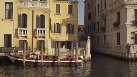 Parked-boats-lit-by-sunrise-in-Canal-Grande-with-small-bridge-in-background,-Venice,-Italy