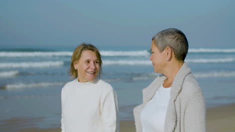 Happy-senior-women-talking-while-walking-along-ocean-coast