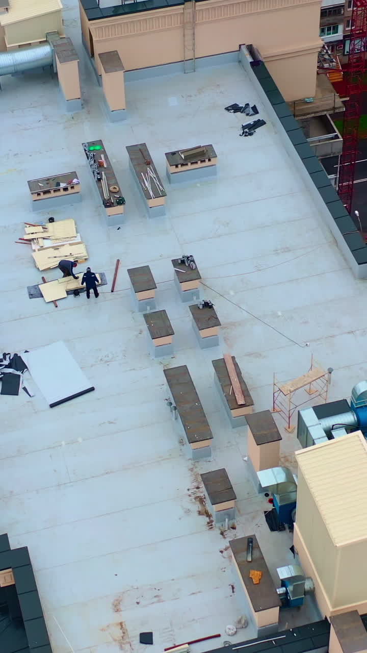 Roof of multistorey building under construction. Modern apartment house builds in the city. Workers build the tower building. Top aerial view. Vertical video