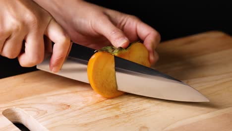 hands carefully slicing a ripe persimmon fruit