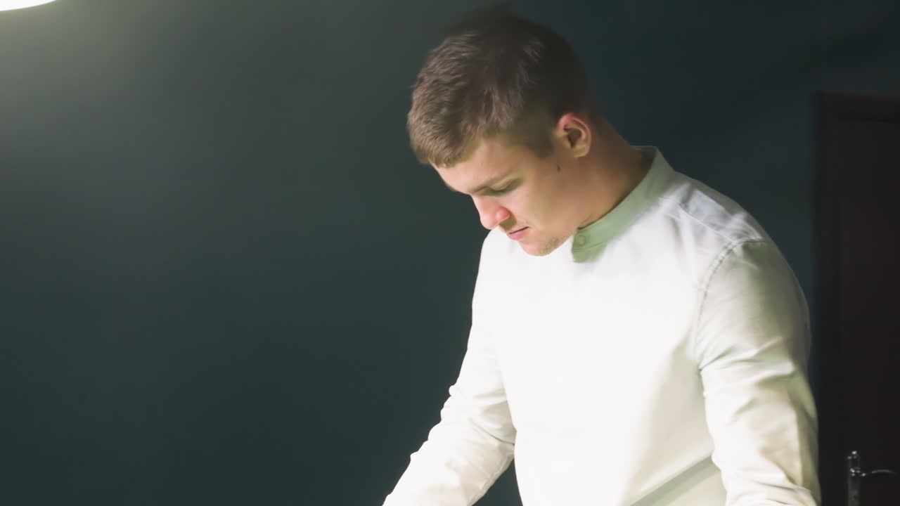 셔츠를 입은 젊은이가 녹색 벽을 가진 빌리어드 방에서 고 큐 스틱을 뽑는 클로즈업. 집중된 표현, 현대적인 인테리어, 희미한 조명, 게임에 대한 세련된 분위기