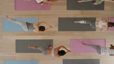 Vista-Superior-Clase-De-Yoga-Mujeres-Sanas-Practicando-Pose-Guerrera-Disfrutando-Del-Estilo-De-Vida-Físico-Haciendo-Ejercicio-En-El-Gimnasio