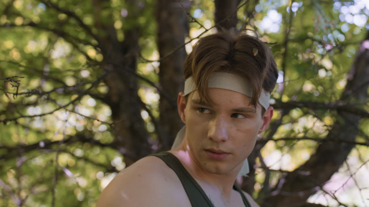 adventurer turning head sharply toward faint forest sound while dry leaf clings to hair, green dappled light through branches casts shadows across shoulder with intense gaze scanning in woodland