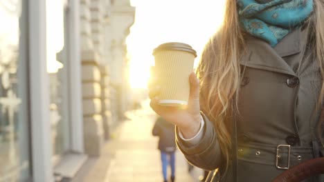 young caucasian woman on a sidewalk with morning coffee in sunshine light