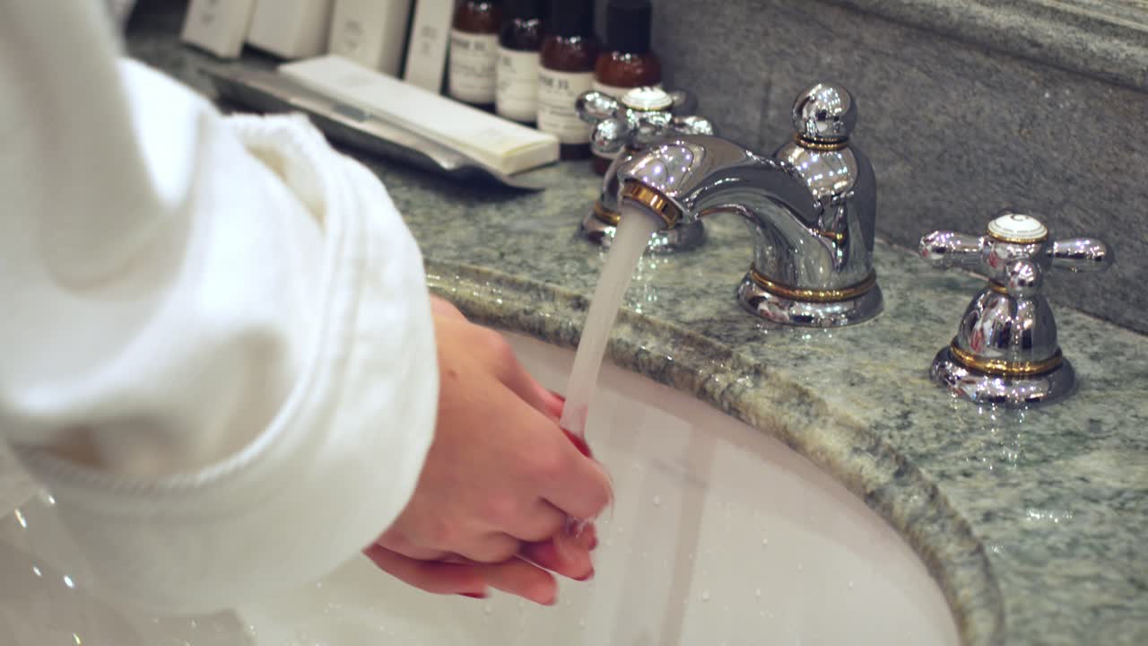 Donna che apre il rubinetto del bagno e si lava le mani in acqua corrente