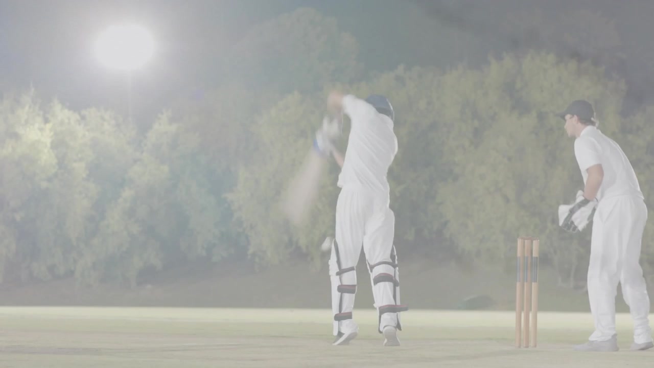 Indisk batsman træder frem og svinger battet, efter at kasteren har leveret bolden under projektørlys for at score