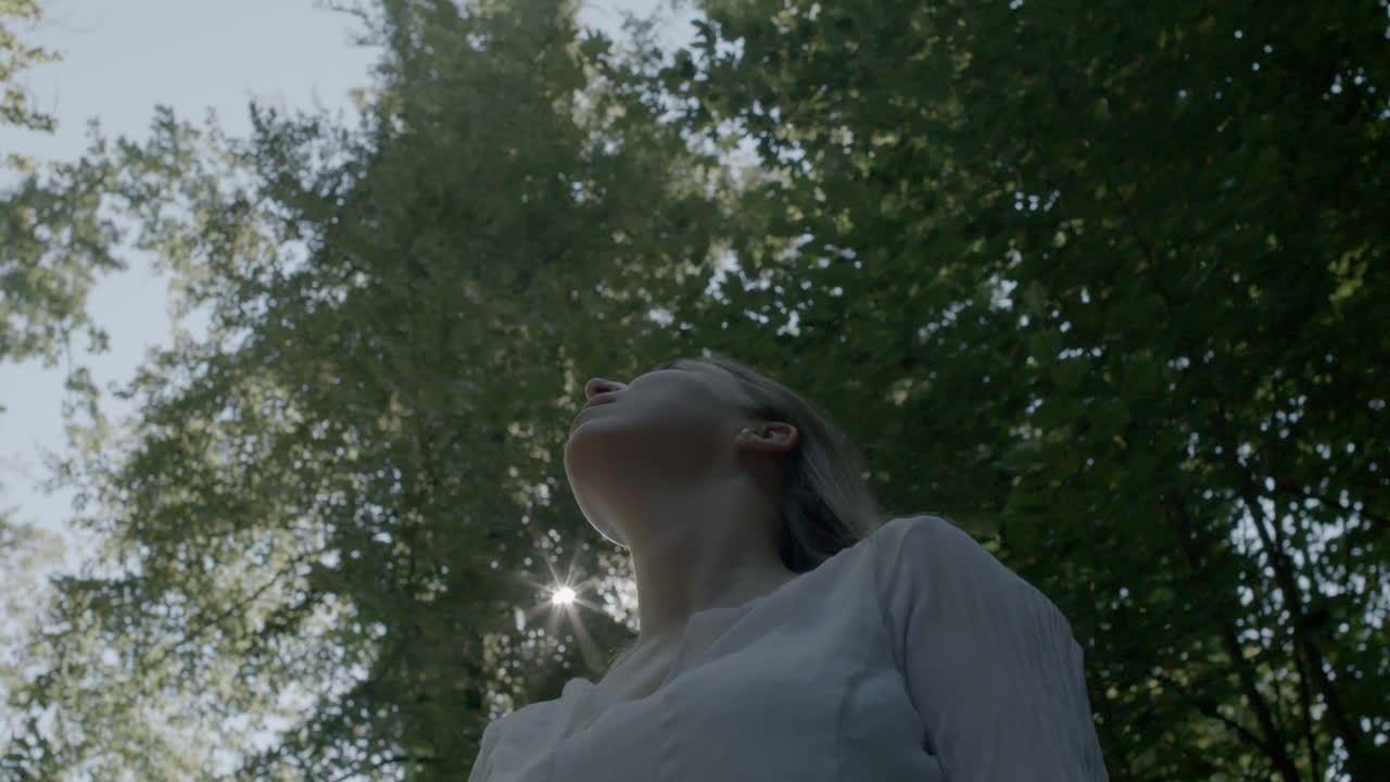 Woman looks up to the sun in park summer