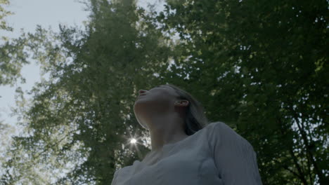 woman looks up to the sun in park summer