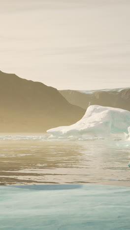 a large iceberg floats in calm water, with mountains in the background