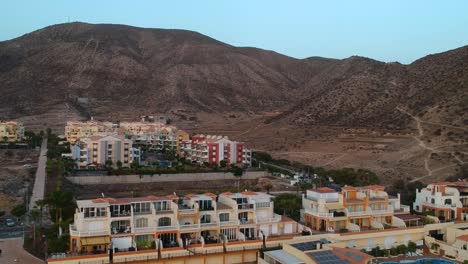 Colorful-resort-buildings-with-balconies-in-Tenerife-island-with-mountain-behind,-aerial-view