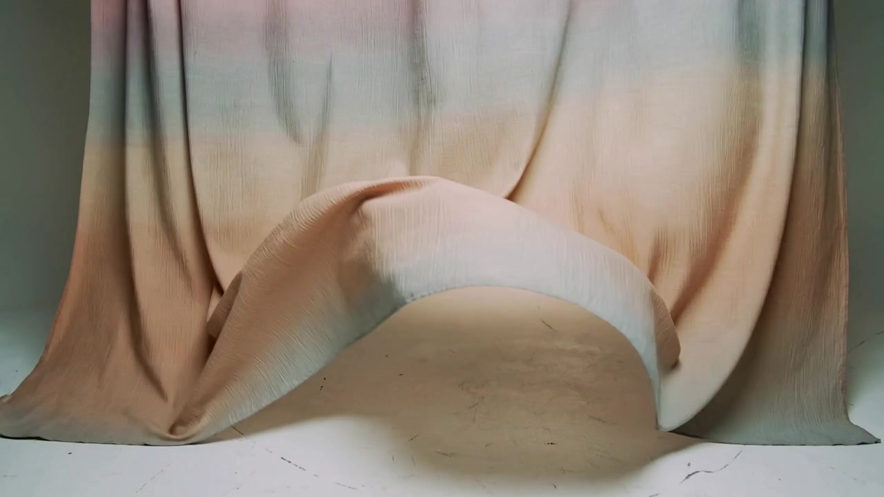 Lifting off-frame hand sending peach fabric arching then settling on studio floor, revealing bulge