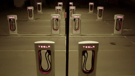 illuminated tesla supercharger charging stations deserted at night, tilt-up