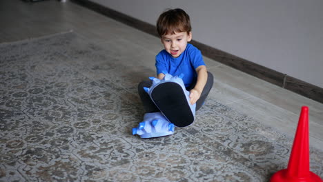 adorable baby boy puts on big funny slippers with claws. little kid playing at home. top view.