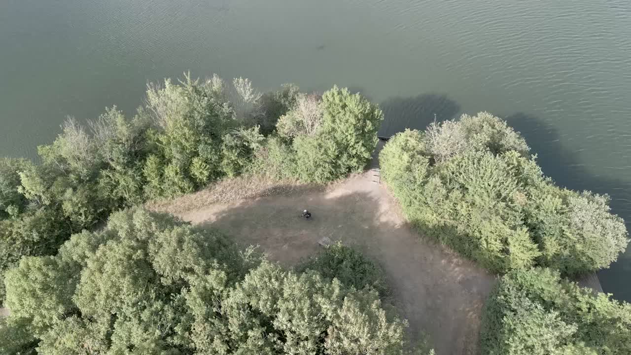 나무가 있는 호수 옆의 귀여운 길을 따라 혼자 자전거를 타는 사람