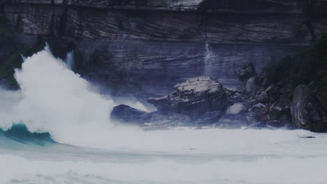 large waves crashing on a rocky shoreline in sydney, australia, with turbulent water and mist