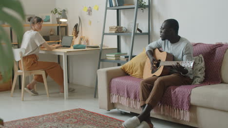 woman using laptop while husband playing guitar and singing at home