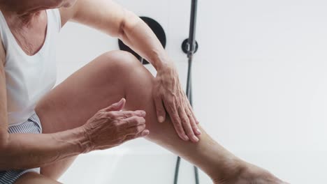 unrecognizable senior woman applying moisturizing cream on legs