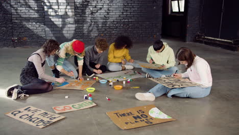 young environmental activists painting placards sitting on the floor