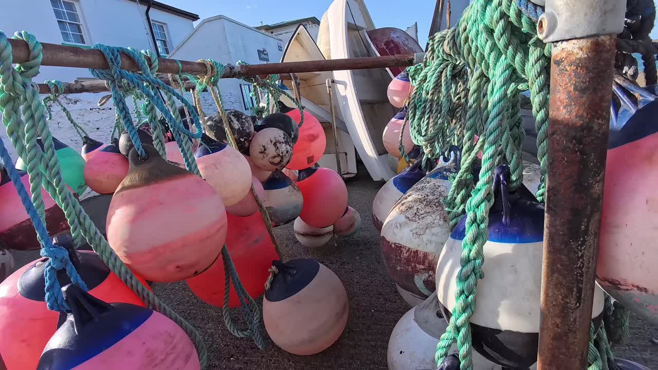 Varias boyas de pesca coloridas colgando en una marina galesa, atadas con cuerda cerca de embarcaciones junto al agua.