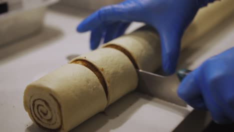 Bäckerhände-Mit-Handschuhen,-Die-Zimtbrötchen-Zum-Backen-In-Der-Bäckereiküche-Schneiden