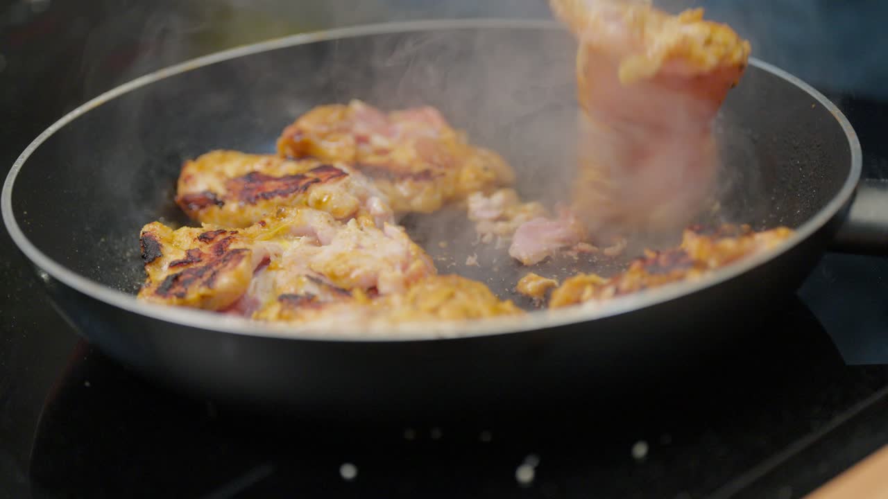 Una persona usa le pinze per girare pezzi di pollo marinato che si stanno dorando in una padella