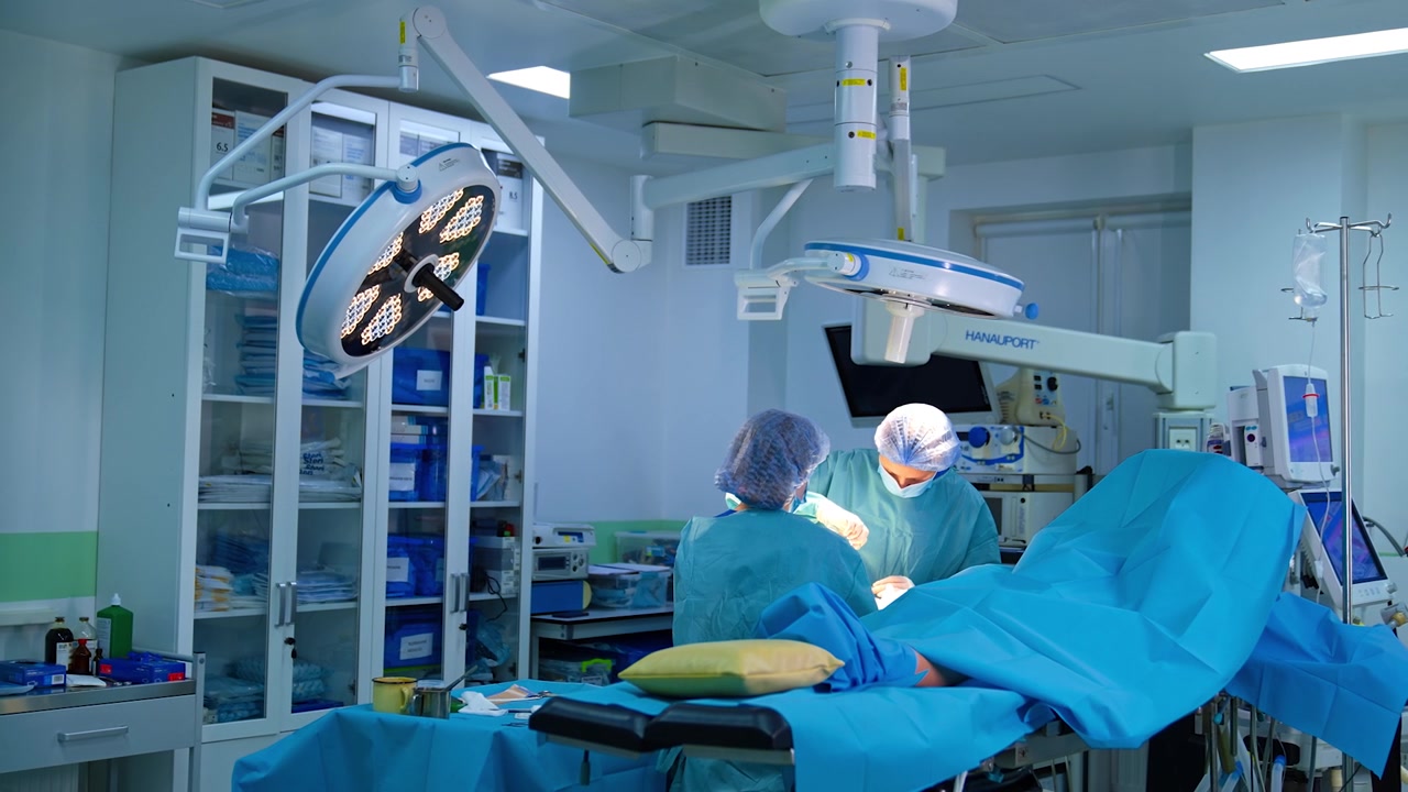Two female medics work in the modern surgery room with diverse advanced equipment. Footage at the doors to an operating theatre.
