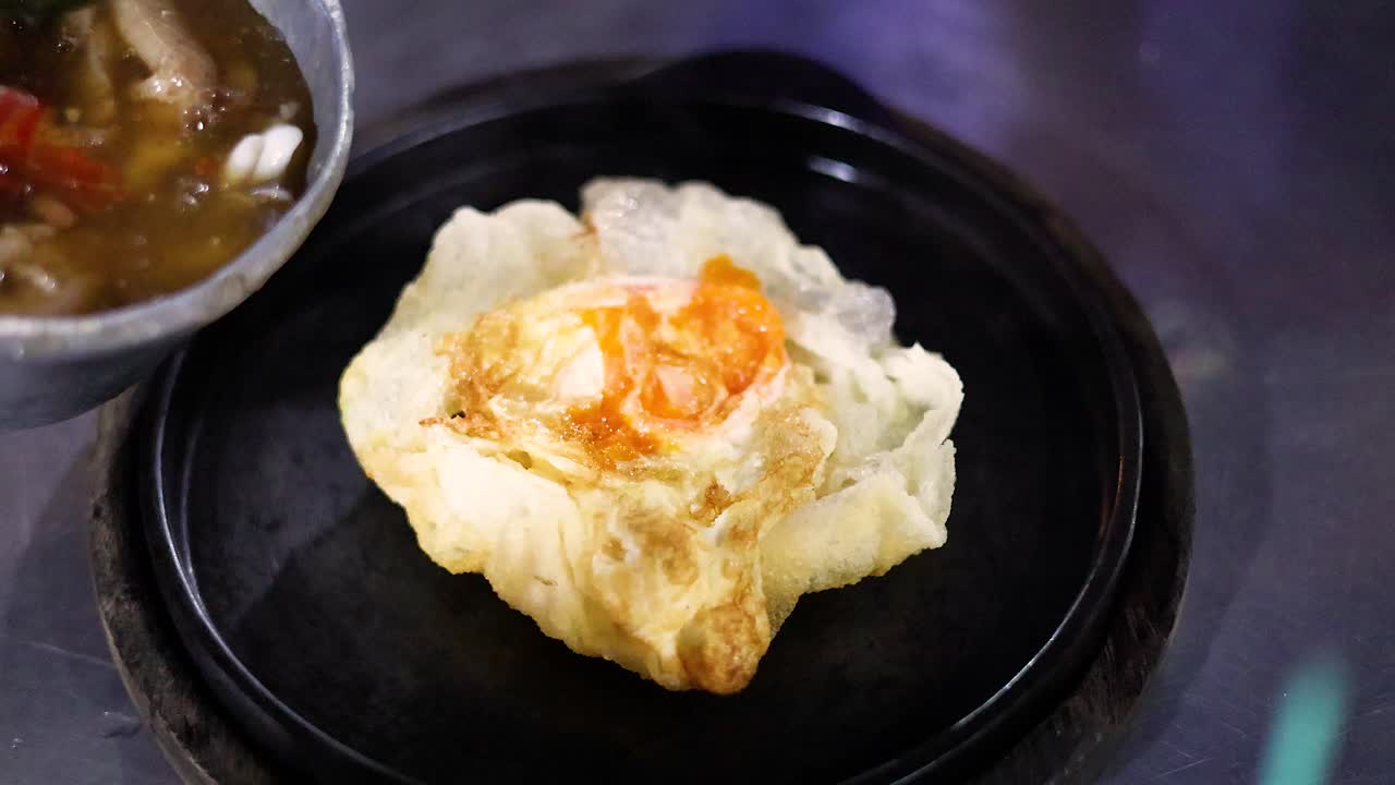 Street vendor pours savory sauce onto crispy fried noodles with shrimp under vibrant night lighting