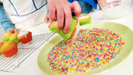 man sticking confectionery on cupcake