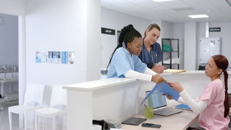 diverse doctors talking to medical recepcionist sitting at front desk at hospital, slow motion